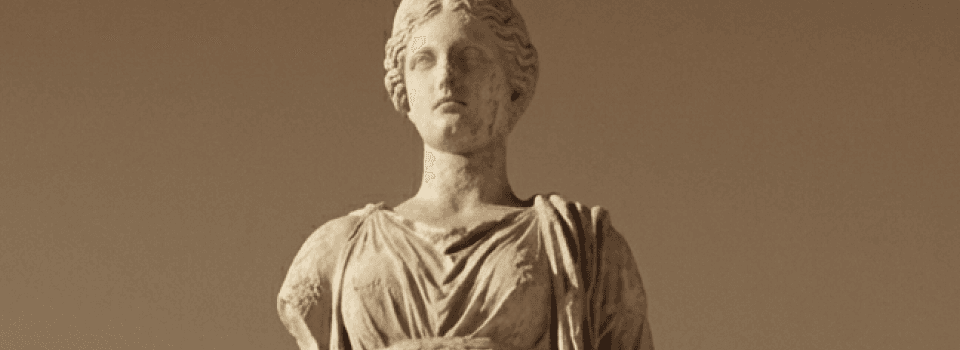 Ancient stone statue of a woman with a serene expression, draped in classical robes, against a warm brown background.